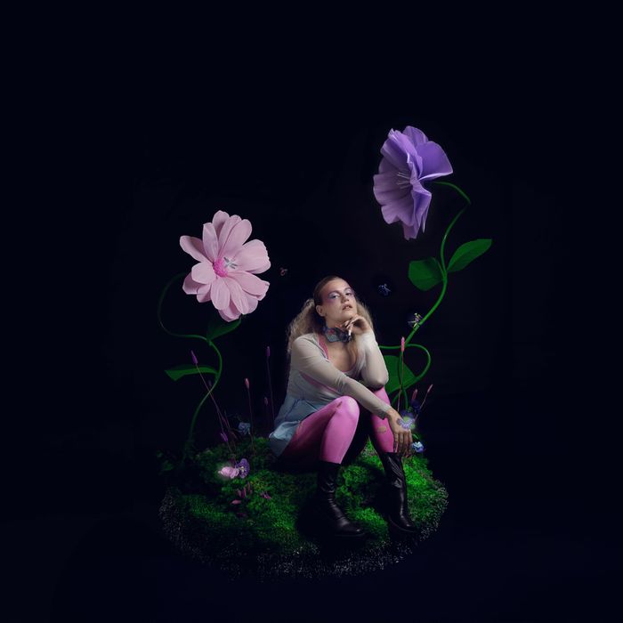 Portrait de Louisadonna, assise sur de l’herbe et entourée de grandes fleurs colorées, modélisées en 3D.