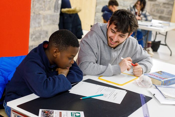 Un jeune adulte souriant aide un enfant à faire ses devoirs.