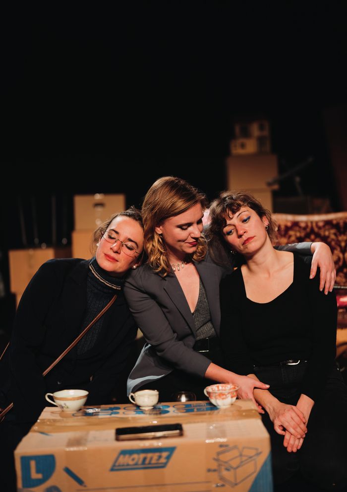 Trois jeunes femmes assises sur un canapé . Devant elles, un carton de déménagement avec trois jolies tasses à thé dessus
