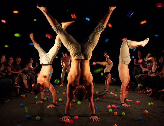© Andy Phillipson Des acrobates sont en équilibre sur les mains pendant que le public leur jette des balles de couleur dessus