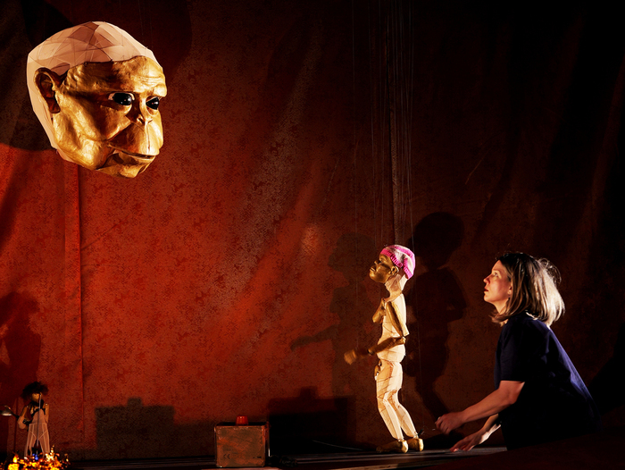 Spécimen (c) Cie Arnica Une comédienne et une marionnette de table font face a une grosse tête d'un personnage préhistorique en marionnette à fils.