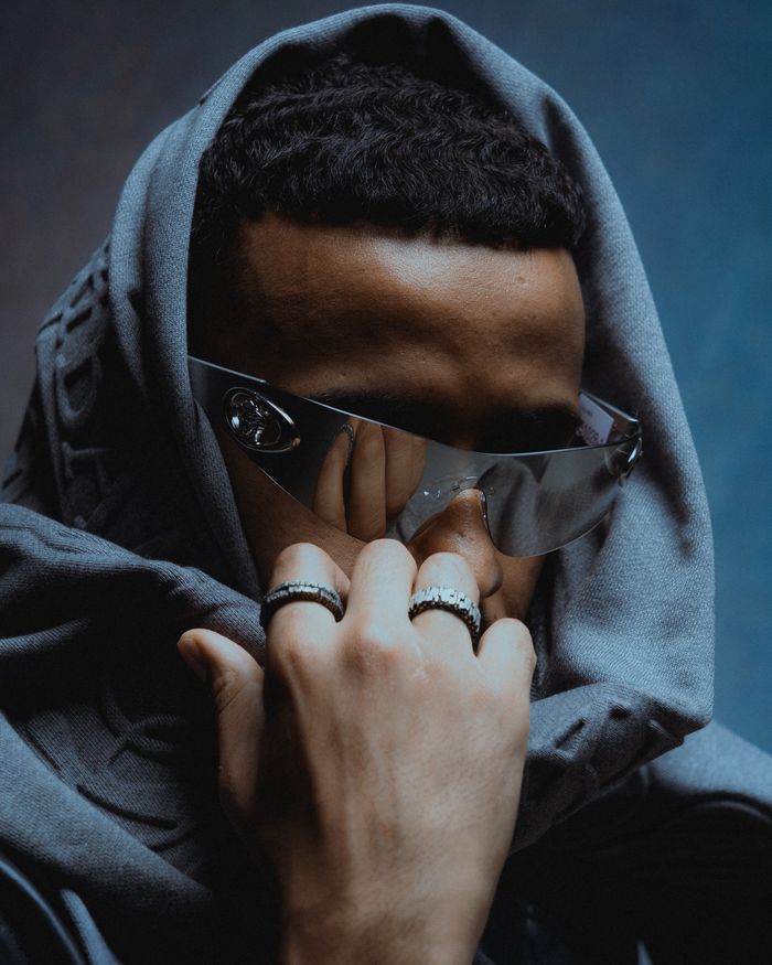 Photo centrée sur Stormy, portant des lunettes et un hoodie. Son regard, à la fois mystérieux et perçant, domine l’image.