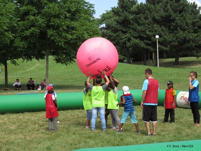 Shev123 Un groupe d'enfant en train de jouer avec un ballon rose gigantesque, tenu au-dessus de leurs têtes.