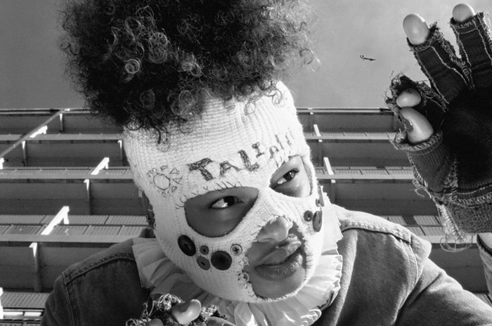 Photo en noire et blanc de la rappeuse, qui porte une cagoule en laine qui lui cache le visage à l'exception des yeux et de la bouche