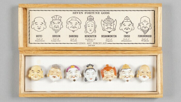 Une boîte en bois dans laquelle se trouve des boutons représentant les visages de dieux japonais.