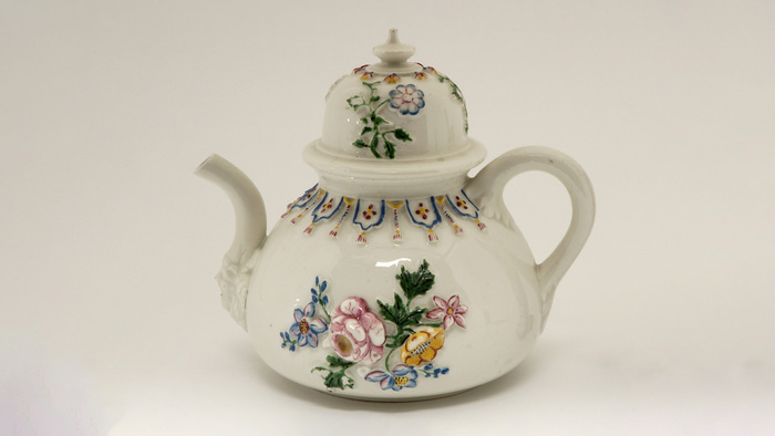Théière en porcelaine sur laquelle sont peintes en relief des fleurs.