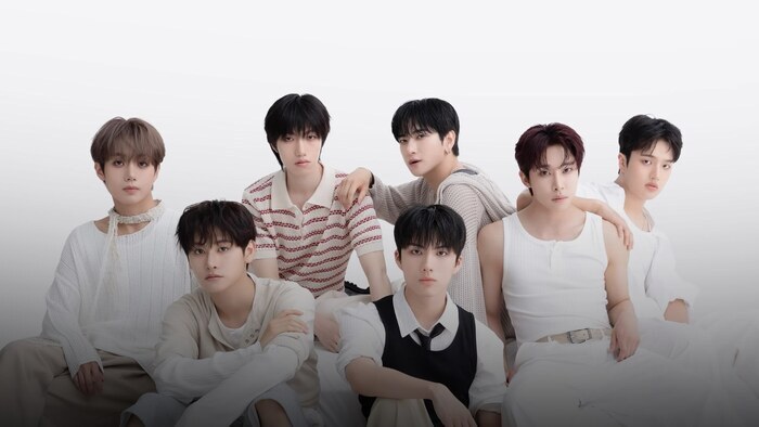 Photo des 7 membres du groupe assis parterre avec un fond blanc en arrière plan