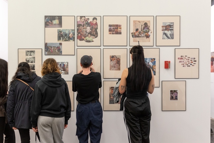 Photo représentant quatre femmes de dos, regardant une série de collages encadrés et accrochés en groupe au mur.