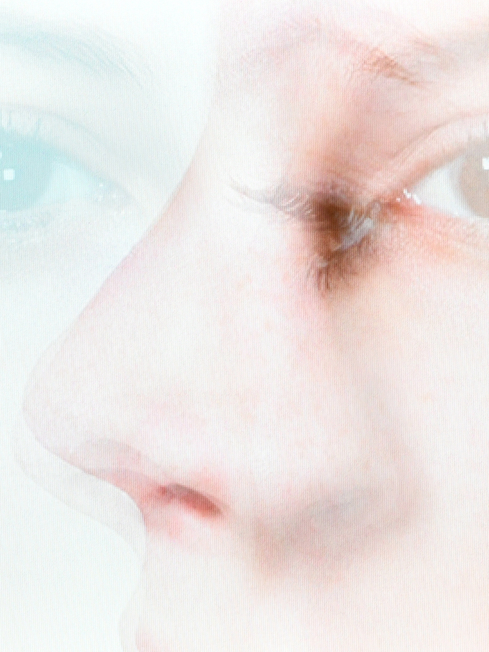 Portrait d'une jeune femme en t-shirt rose dont le visage est presque dissimulé par les branches d'un arbre.