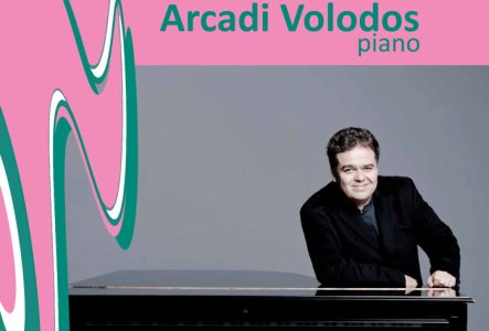 Sur fond rose, Arcadi Volodos posant devant un piano