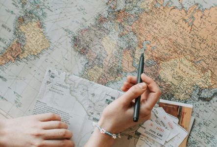 Une personne tient un stylo au dessus d'une carte du monde ouverte