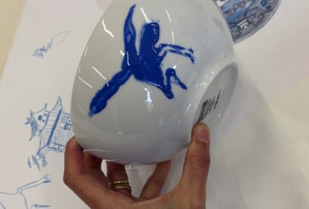 Une personne est en train de dessiner un décor bleu sur une porcelaine.