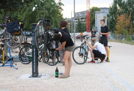 Plusieurs personnes discutant et réparant leur vélo à la borne d'auto-réparation de la voie verte