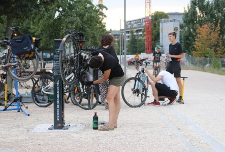 Plusieurs personnes discutant et réparant leur vélo à la borne d'auto-réparation de la voie verte
