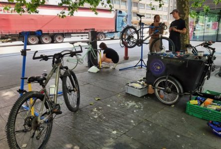 Plusieurs personnes discutant et réparant leur vélo à la borne d'auto-réparation du parvis d'Uni Mail