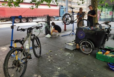 Plusieurs personnes discutant et réparant leur vélo à la borne d'auto-réparation du parvis d'Uni Mail