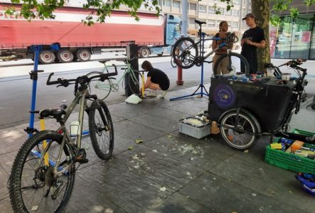 Plusieurs personnes discutant et réparant leur vélo à la borne d'auto-réparation du parvis d'Uni Mail
