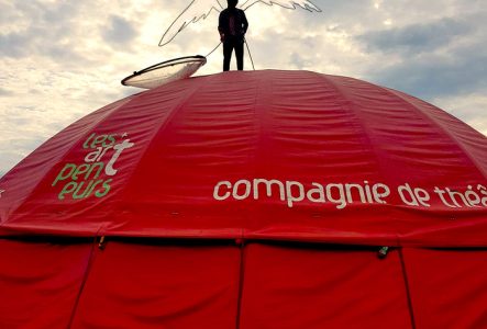Un homme à contre jour se tient sur un chapiteau rouge. Une paire d'ailes est dessinée sur la silhouette.