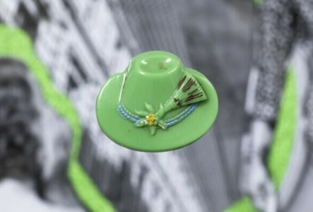 © Rebecca Bowring Un bouton vert pomme en forme de chapeau est disposé sur une image en noir et blanc et légèrement floue représentant des femmes