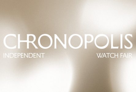 Visuel épuré sur fond de métal brossé aux reflets dorés et champagne. Au centre, le titre CHRONOPOLIS est écrit en lettres capitales blanches et fines. Juste en dessous, les mentions INDEPENDENT (à gauche) et WATCH FAIR (à droite) complètent l'affiche.