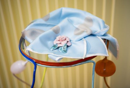 Broche en céramique réalisées par Marie Ducaté. Elle a la forme d'une fleur et est posée sur un foulard de couleur bleu.