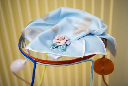 Broche en céramique réalisées par Marie Ducaté. Elle a la forme d'une fleur et est posée sur un foulard de couleur bleu.
