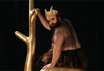 Un homme barbu portant une couronne dorée sur la tête et un pagne tient une (fausse) branche d'arbre dorée.