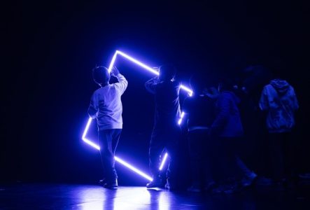 Des enfants en mouvement devant un carré fait de neon bleu
