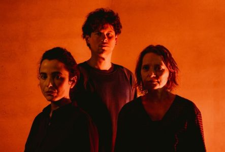 Portrait de trois comédien.nes sous une lumière rouge.