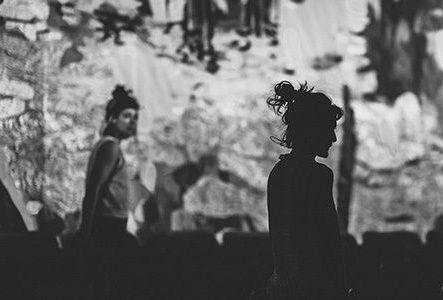 Une photo en noir et blanc avec deux personnes devant une fresque en tissu.