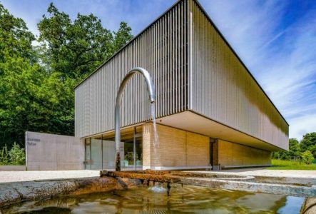 Bâtiment moderne de la Maison du Futur à Vessy, avec fontaine au premier plan et arbres en arrière-plan.