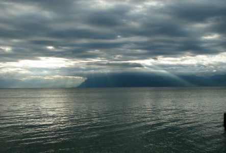 Photo du Léman sous un ciel couvert à travers lequel les rayons du soleil passent.