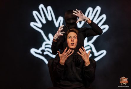 Deux personnes (une femme bien visible et un homme avec un masque noir) montrant leurs mains et il y a quatre mains lumineuses derrière eux