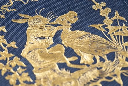 Broderie au fil d'or sur un tissu bleu représentant un lapin tenant un canard