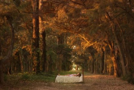 Une femme est couchée sur un lit, au milieu d'une forêt.