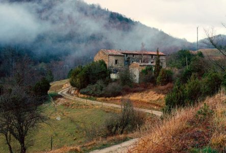 Photo d'une vieille maison sur une colline, avec une route qui y mène et de la brume