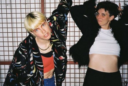 Deux femmes posent devant un grillage.