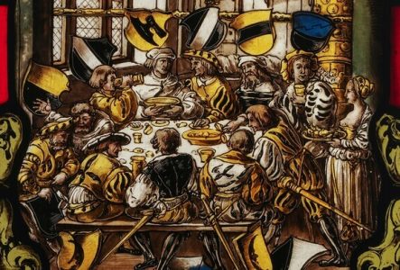 © Atelier Girardet Vitrail représentant un festin médiéval : on y voit des hommes autour du table en train de manger et de boire. Il y a une dominance de jaune et de noir.