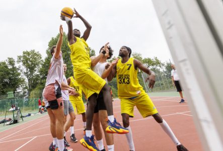 Cette image capture une action de jeu intense lors d'un match de basket-ball 3x3 en extérieur.
Un joueur s'élève très haut dans les airs pour tenter un tir en suspension.