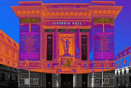 Projection de noms de compositrices en mapping sur la façade du Victoria Hall en teintes oranges et violettes.