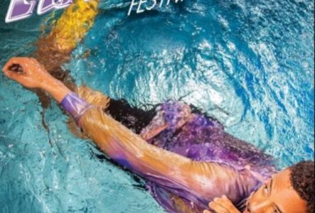 L'image montre un homme immergé dans une eau de piscine d'un bleu. Il porte une chemise aux nuances violettes, lilas et jaunes.