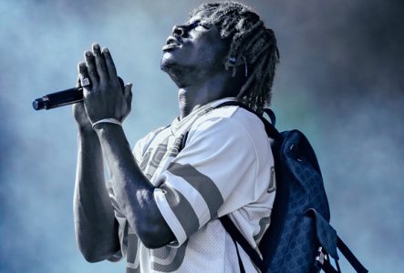 Photo de l'artiste sur scène de profil avec un micro entre ses mains et un sac à dos