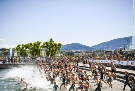 Cette image montre le départ impressionnant du Triathlon de Genève.
On voit une foule d'athlètes se jeter dans le lac Léman.