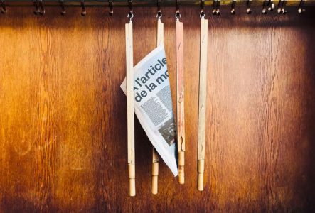 Une photo de quatre baguettes de journaux suspendus à des crochets, dont une avec un journal sur lequel on devine le titre du spectacle.