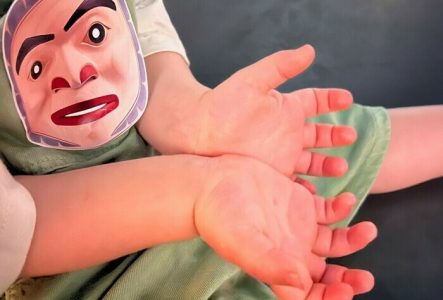 DR AHO MEG Les paumes des mains d'un enfant qui a un autocollant collé sur son habit. cet autocollant représente le masque d'un prince.