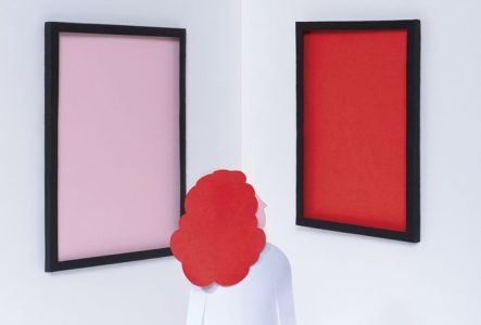 un personne de dos regarde un coin de salle sur les murs de laquelle sont fixés 4 tableaux sans image, dont l'intérieur est coloré en rose, rouge, bleu clair et bleu foncé.
