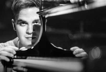 Portrait en noir et blanc de l'artiste qui se tient à hauteur du clavier de son piano