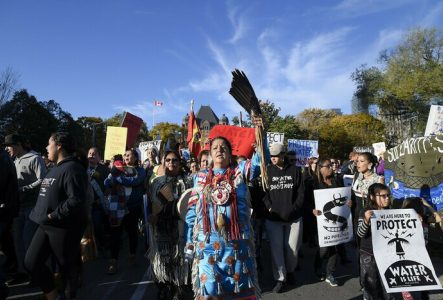 Manifestation, pancartes, slogans, défense de l’eau, peuples autochtones, vêtements traditionnels, solidarité, ciel bleu, drapeau canadien.