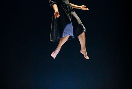 Sur scène, une femme flotte dans les airs, les yeux fermés et les bras ouverts.