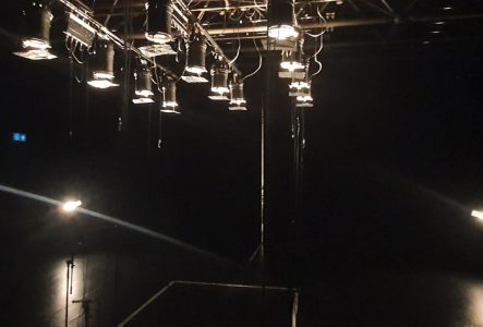 Cette image montre une dizaine de projecteurs de théâtre dirigés vers une scène vide.